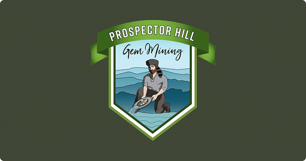 A logo with a green shield showing a prospector panning for gems in water, with the text Prospector Hill Gem Mining on a green ribbon above.
